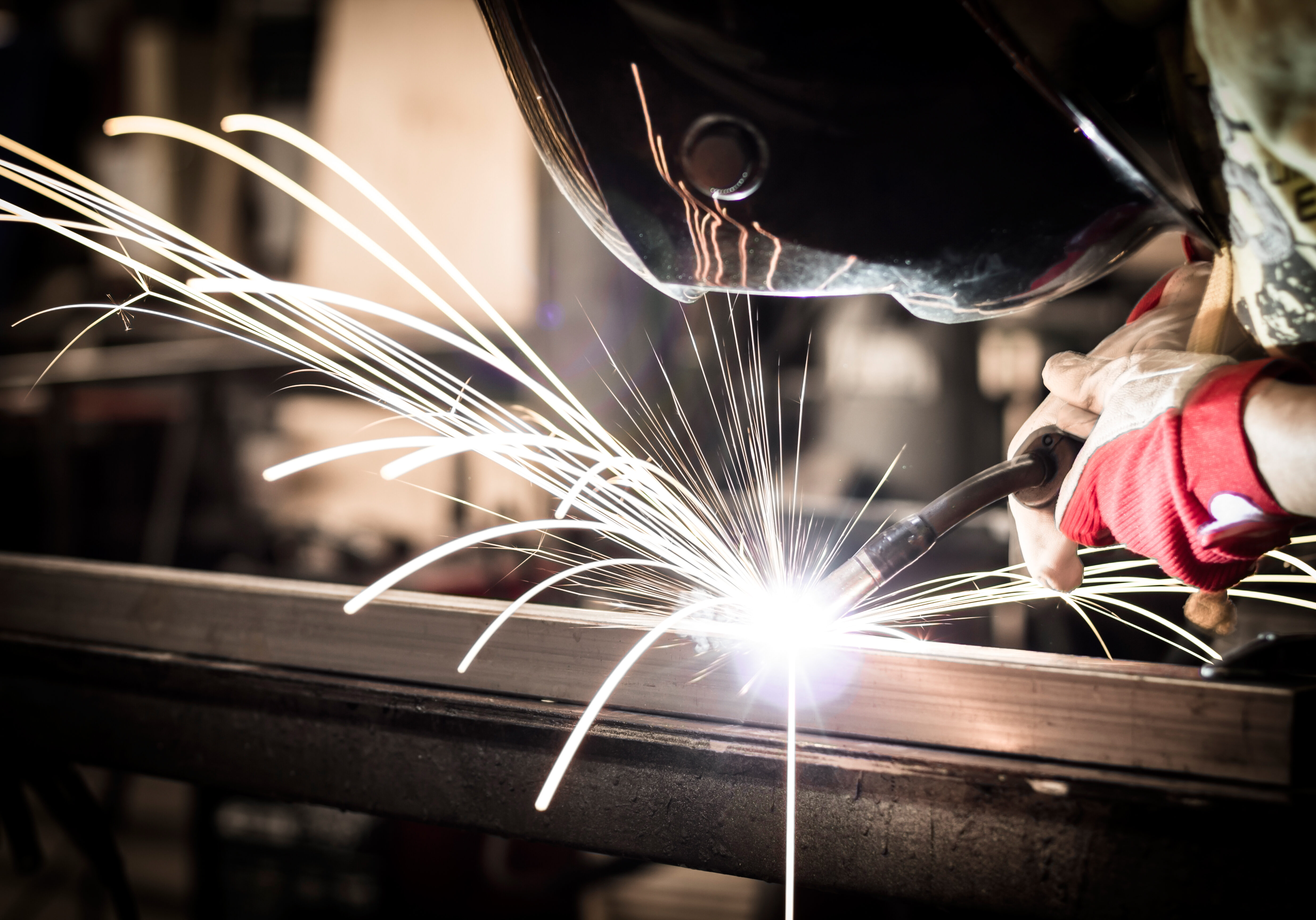 Employee welding steel tubes with sparks in factory.